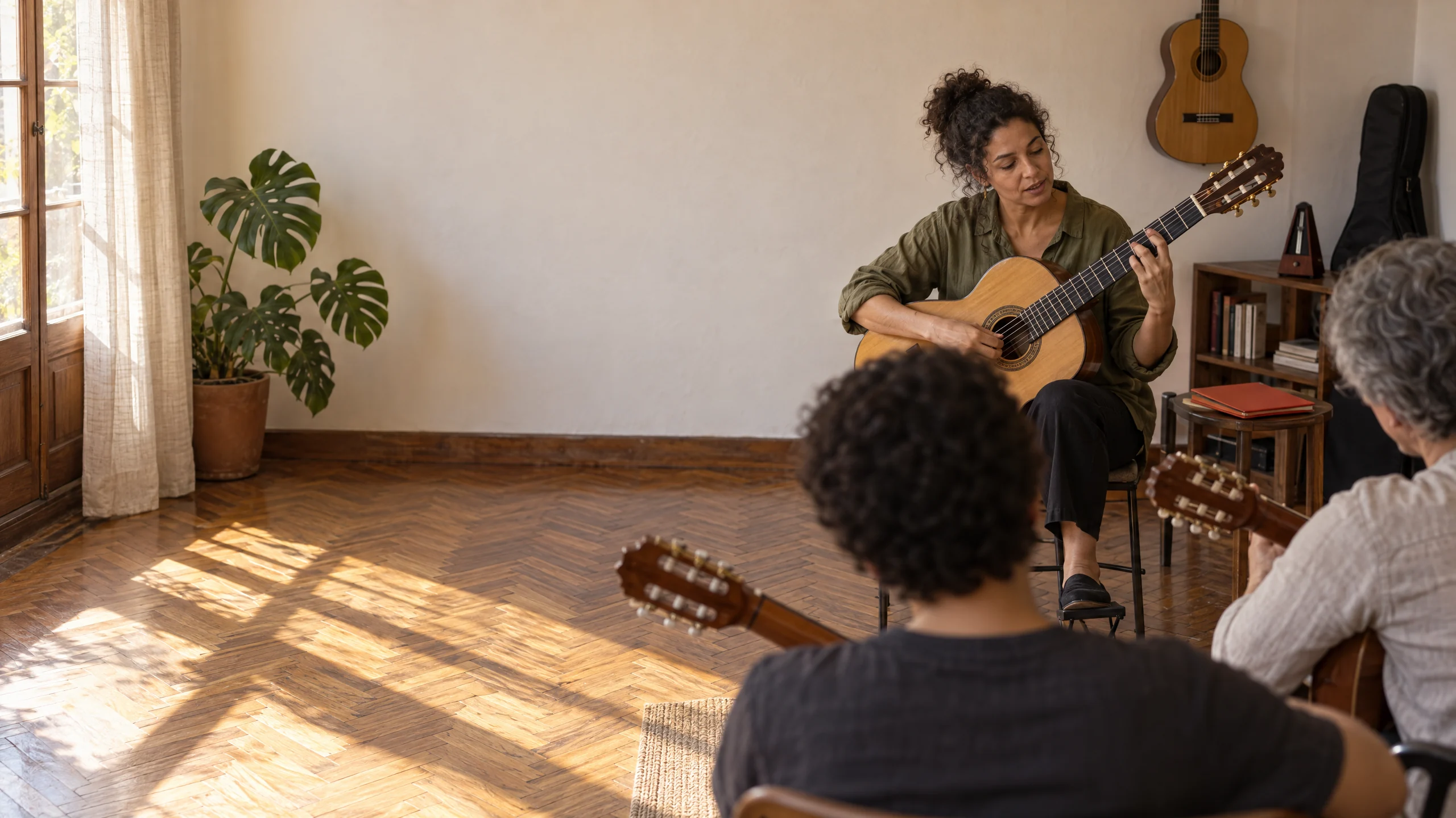 Profesora de guitarra tocando el acorde para el grupo presencial, con dos alumnos de espaldas, cada uno con su propia guitarra.